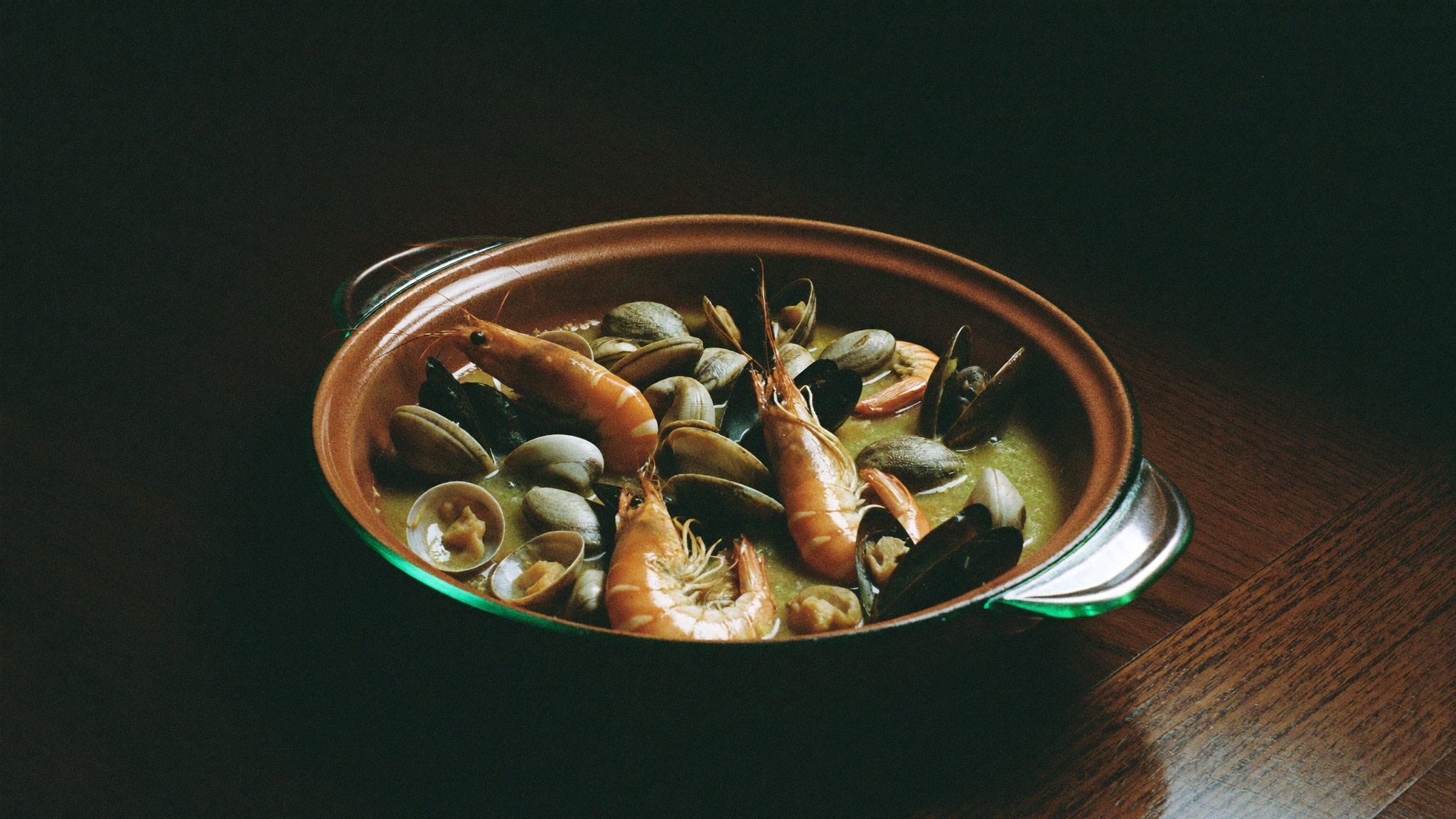 Tacho de barro com marisco húmido à luz quente, sobre mesa escura